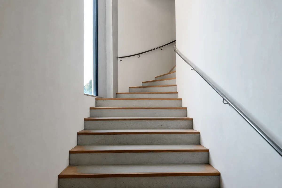 Escalier intérieur en béton et bois d&rsquo;un petit immeuble d&rsquo;entreprise suisse, rampe métallique fine